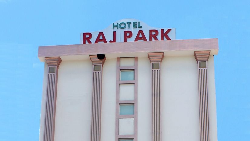Facade of Raj Park hotel with blue sky in the background and a car parked in the entrance of the hotel