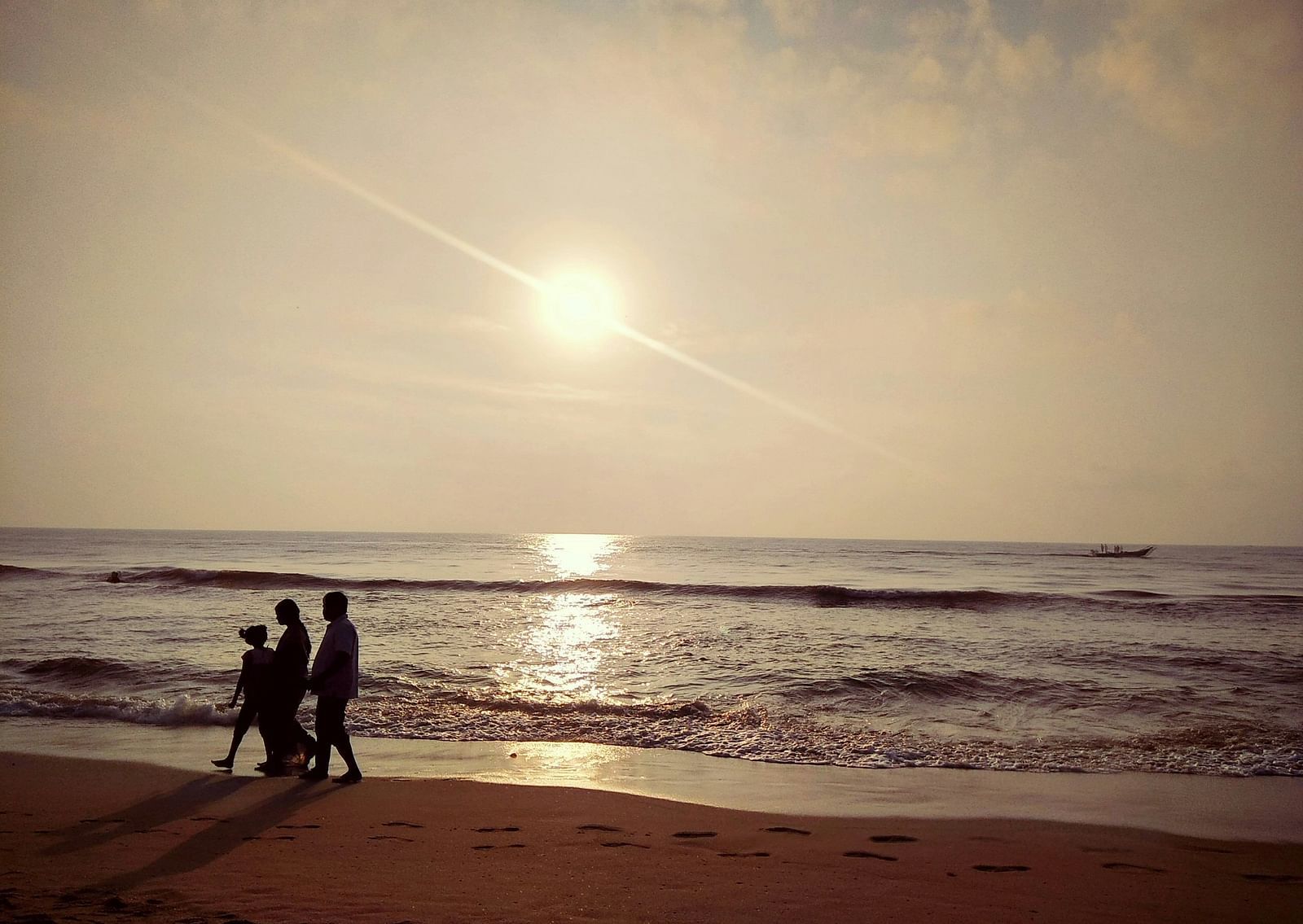 A family of three walking on the beach next to the waves with the sun setting in the background.
