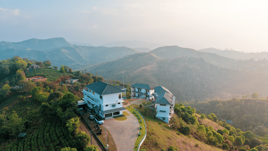 An aerial view of Abad Silver Mist, Vagamon, the best family resorts in Vagamon, on a grassy hilltop surrounded by tea plantations and rolling mountains