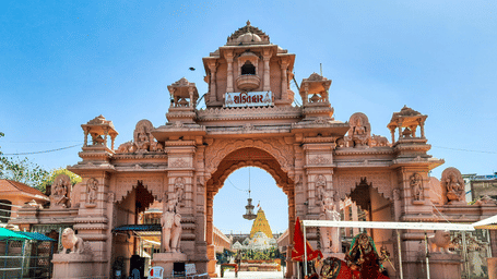 Ornate entrance gateway at Ambaji Temple, one of the best places to visit in Ambaji, featuring intricate carvings, sandstone architecture, steps, and pilgrims gathered beneath clear blue skies.