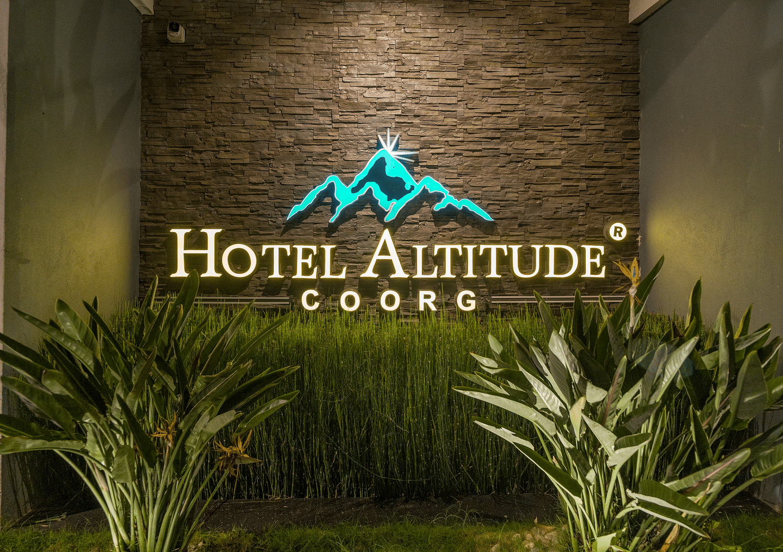 A wall with Hotel Altitude written on it and with plants in front at Hotel Altitude, Madikeri.