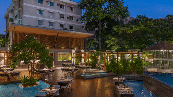 An outdoor swimming pool with a bar and lounge area, surrounded by lush greenery.