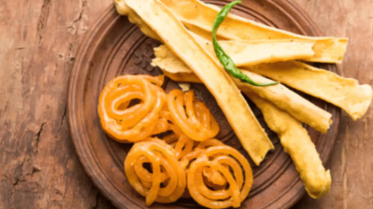 A plate of crispy fafda paired with sweet jalebi, garnished with a vibrant green chili on top for a spicy kick!