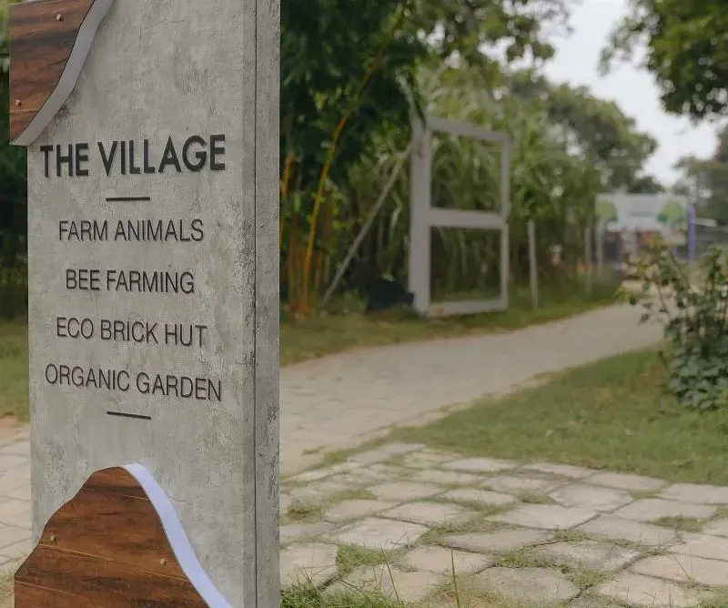 Stone sign reading  The Village near a pathway and greenery at Karma Chalets.