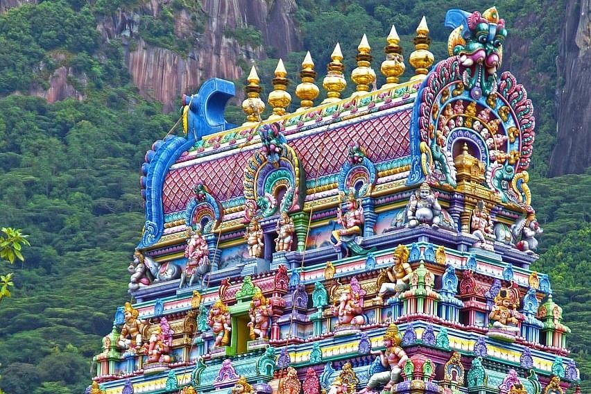 Colorful close-up of an ornately carved Dravidian-style temple with lush hills in the background.