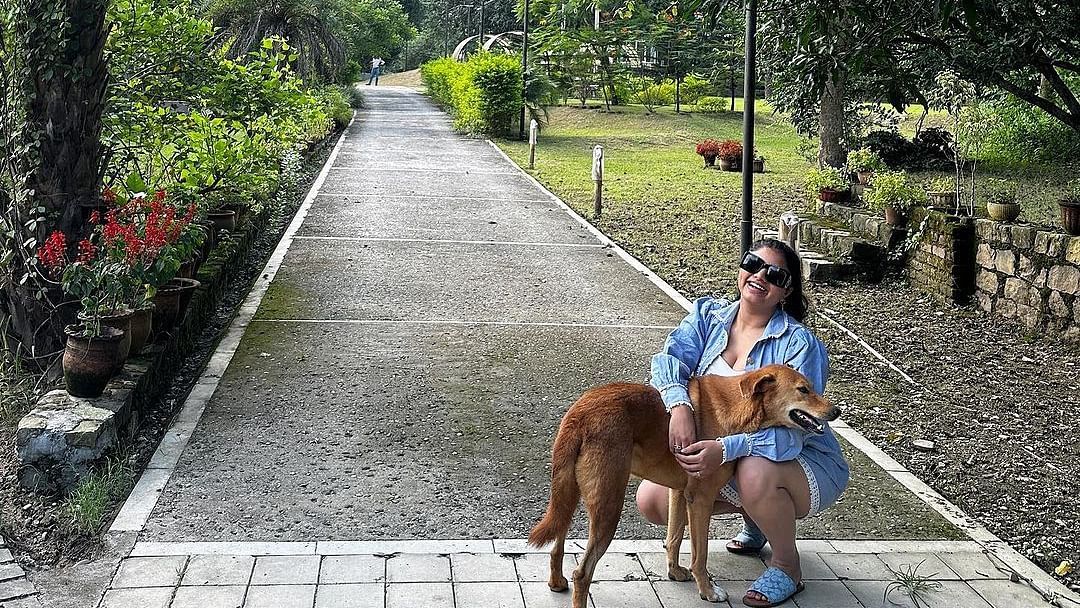 A woman petting a dog on a pathway surrounded by greenery at the Sylvan Retreat, Dehradun.