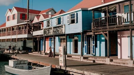 A waterfront road featuring colourful buildings and boats docked at the pier on a sunny day.