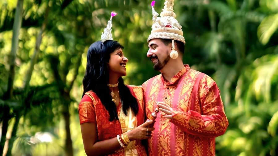 An Indian couple in traditional attire poses outdoors amidst lush greenery, with the groom wearing a turban and the bride in a matching outfit