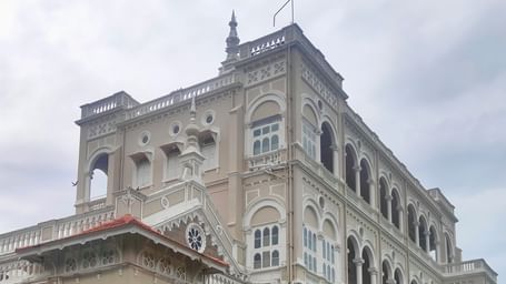 Grand heritage building with arched windows, tiled roof, and garden area.