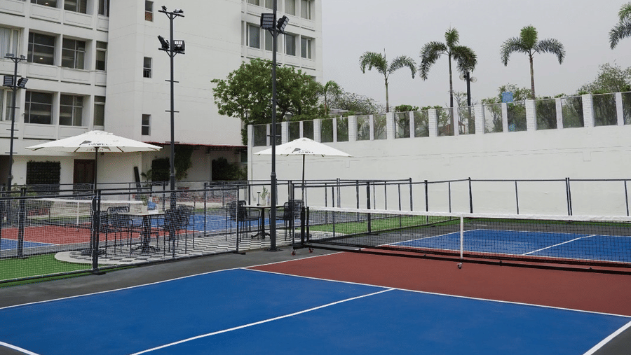 A high-rise hotel building overlooking an outdoor sports court with marked play areas and boundary fencing at Clarks Avadh, Lucknow.