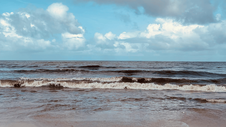 An overview of waves overlapping on the golden sandy shoreline of a beach with blue sky in the background.