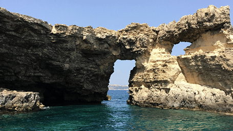 Natural rock arch, like the one at Devil’s Bridge, Antigua, rising from clear turquoise water along a rugged coastline