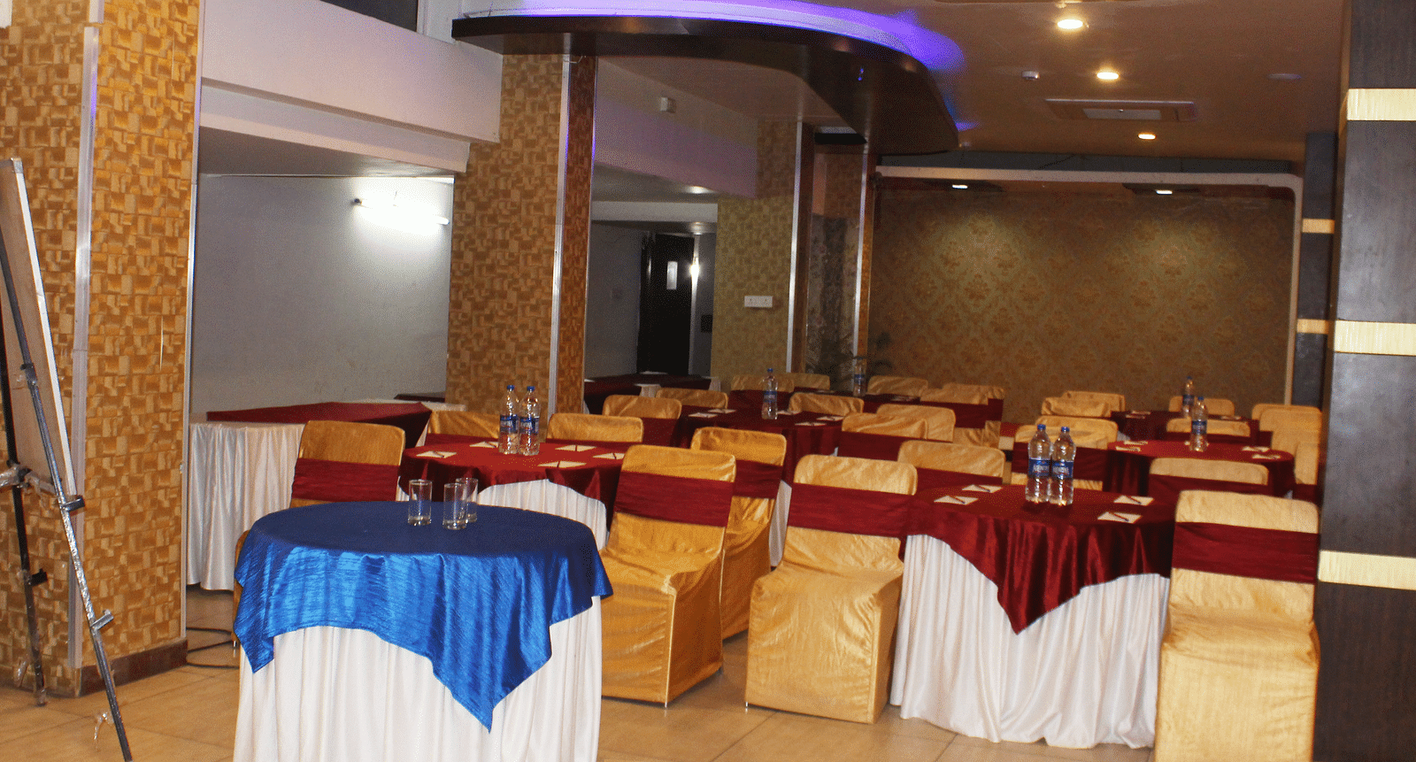 A banquet hall with round tables covered in blue and red cloths and amber-coloured chairs - TGI Apple Inn, Jaipur 