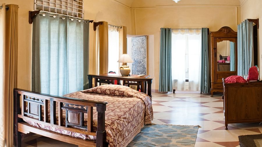 A bedroom with a bed, a table, and a wardrobe in Tijara Fort-Palace - 19th Century, Alwar.