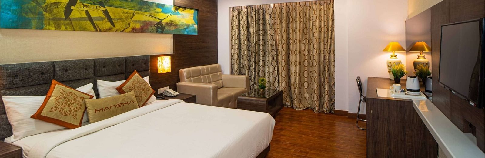 A room with a bed, a sofa, a wall-mounted television, and a ceiling fan at Mansha Hotel Regency.