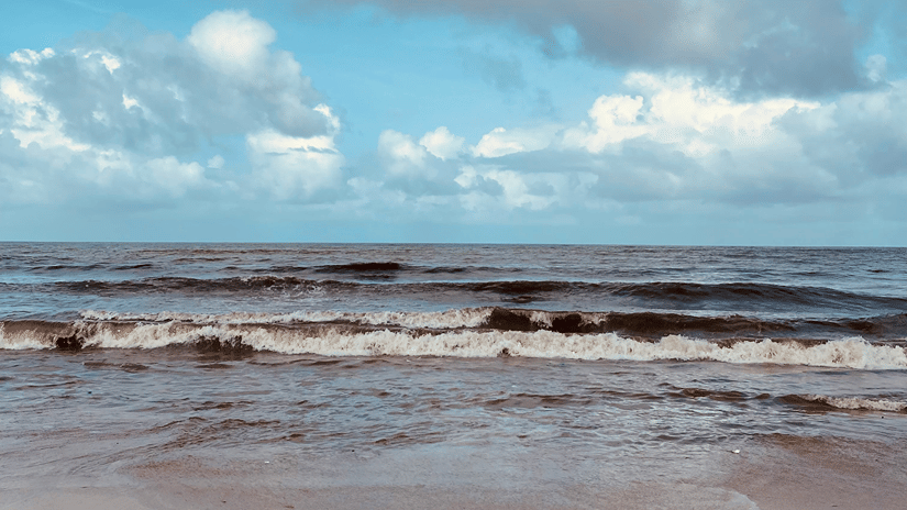 An overview of waves overlapping on the golden sandy shoreline of a beach with blue sky in the background.