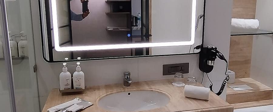 Interiors of a modern bathroom in an executive room at Mirage Hotel, featuring the sink area, an illuminated mirror and a ceramic bathtub.