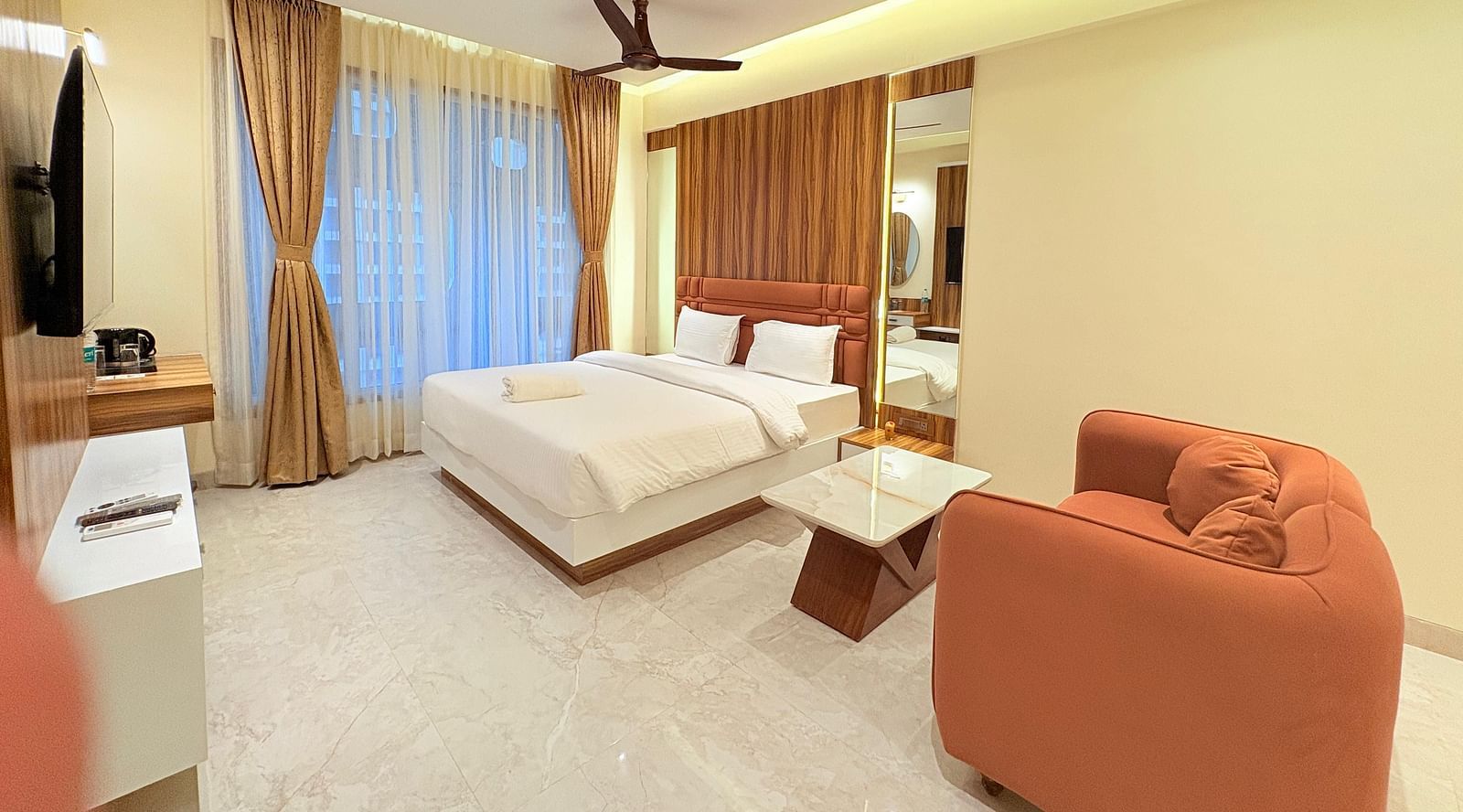 A spacious bedroom featuring a king size bed, a large sofa, and a wall-mounted television at Hotel Mumbai House, Vashi