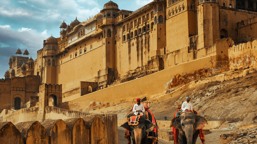 A side view of the Amer Fort in the background with tourists riding elephants along the pathway at the base of the fortress.