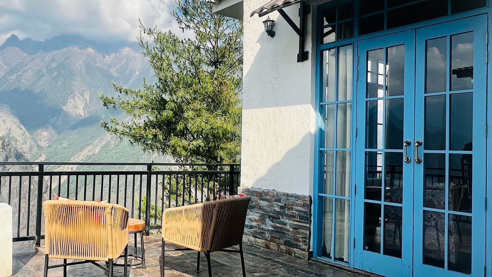 Outdoor patio of a luxury hotel room with comfortable seating and breathtaking mountain views through large glass doors | Faraway Cottages, Auli