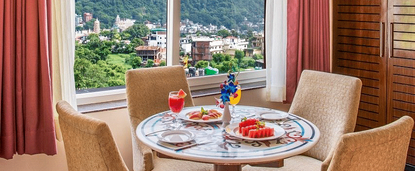A dining table surrounded with four cushioned chairs overlooking beautiful mountain views from the window of the suite at Regenta Inn DLS.