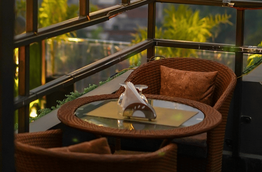 Two chairs facing each other on a terrace with warm lights besides it on a late evening.