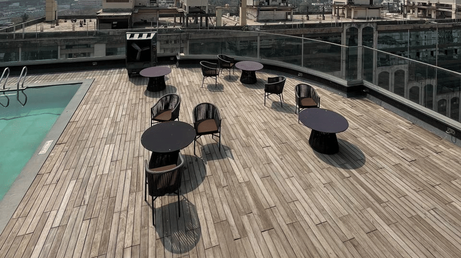 Panoramic high-angle view of a rooftop terrace with small tables and a distant city skyline under a clear sky.