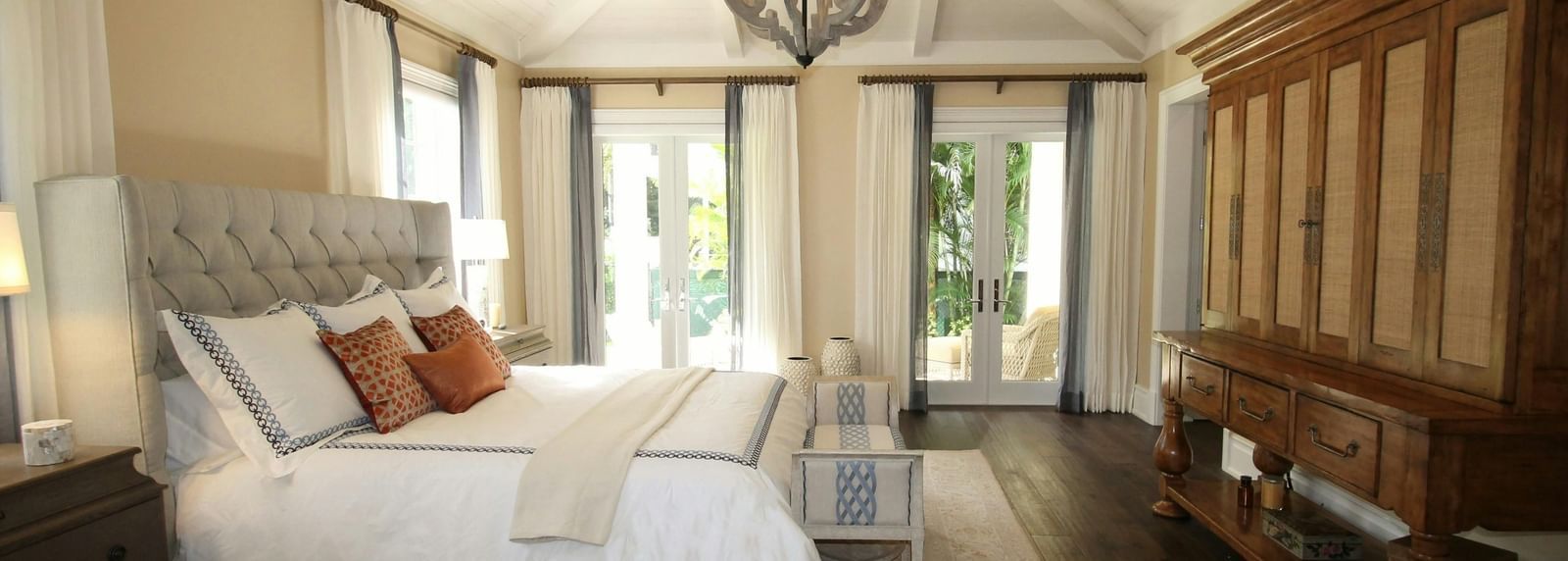 Elegant bedroom with vaulted ceiling, large bed, chandelier, wooden wardrobe, and balcony doors letting in natural light.