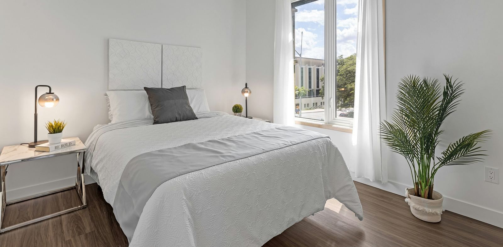 A bedroom with a large window and a potted plant beside it, bringing in natural light and greenery.