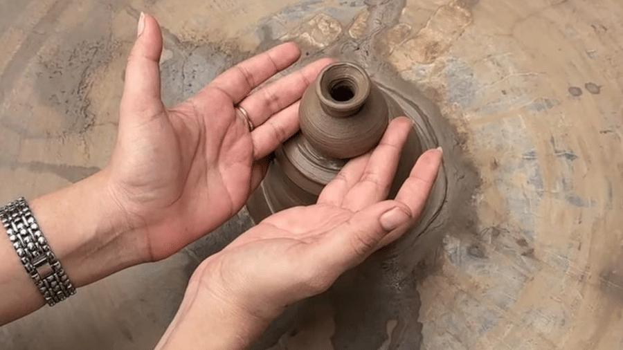 Hands shape clay on a spinning pottery wheel to create a small pot at Amantra Shilpi Resort, Udaipur.