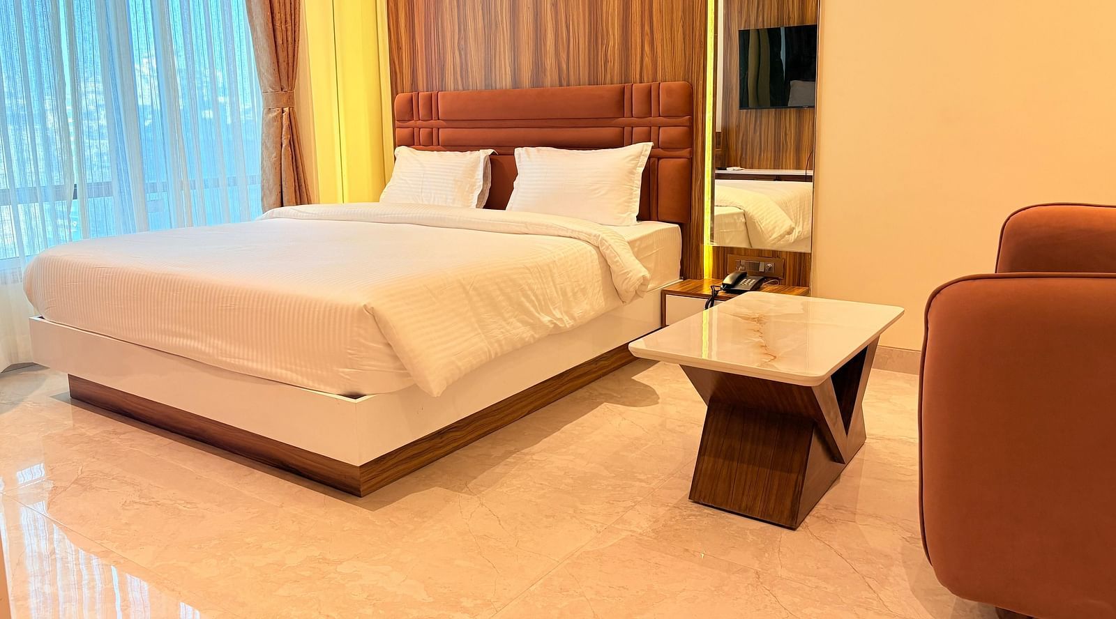 A bed with a wooden headboard and a television reflected in the mirror at Hotel Mumbai House, Vashi.