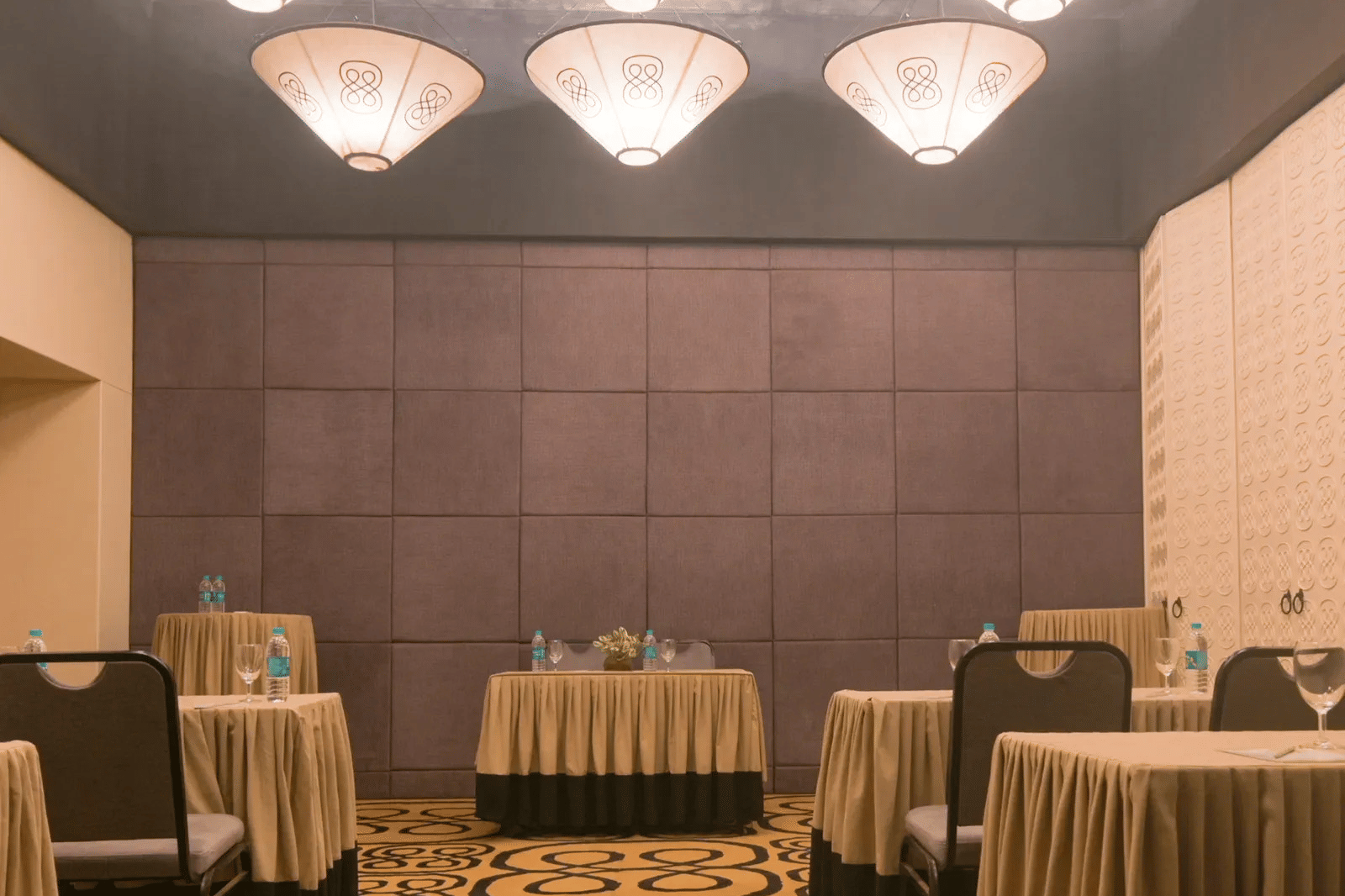 Dholavira banquet hall arranged with draped tables, chairs, patterned carpeting, and overhead warm pendant lights at 3102bce - A Vedic Resort by Lindsay.