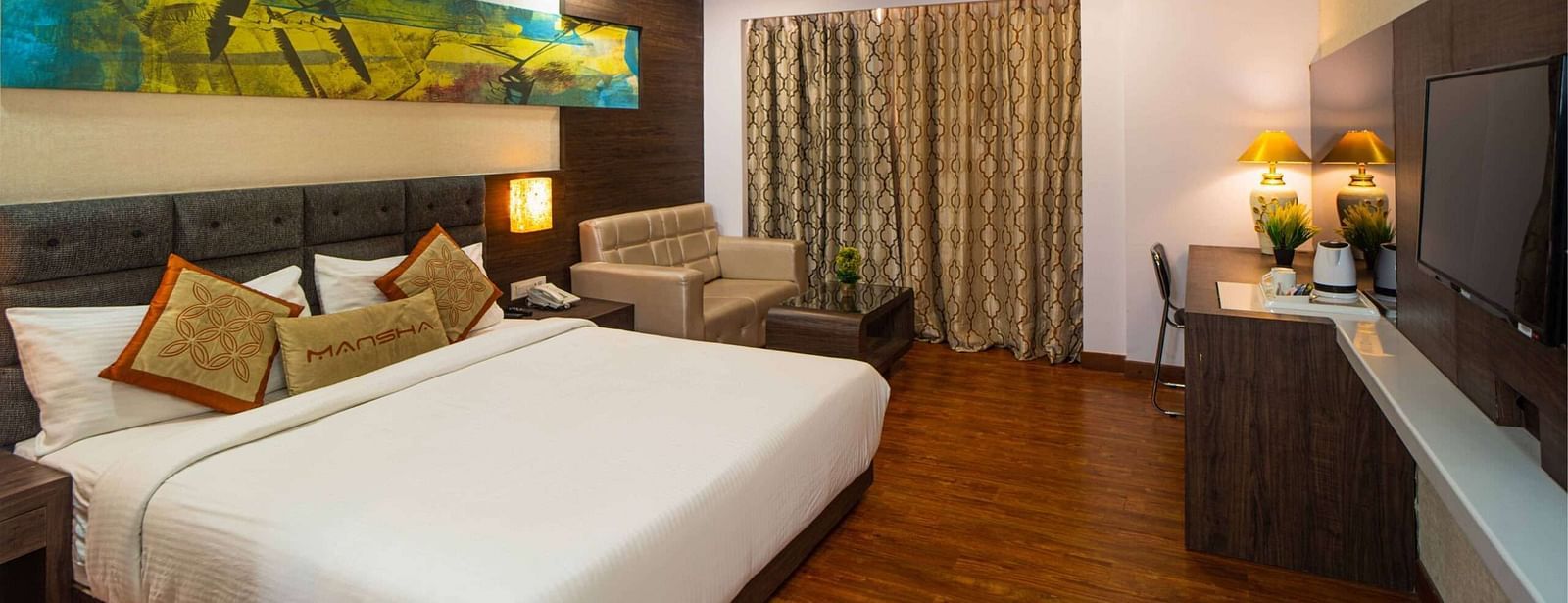 A room with a bed, a sofa, a wall-mounted television, and a ceiling fan at Mansha Hotel Regency.
