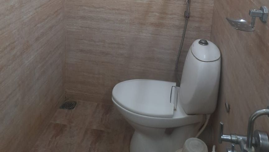 Compact bathroom at Udipi Home, Egmore, Chennai with wall-mounted toilet and overhead shower against beige tiled walls.