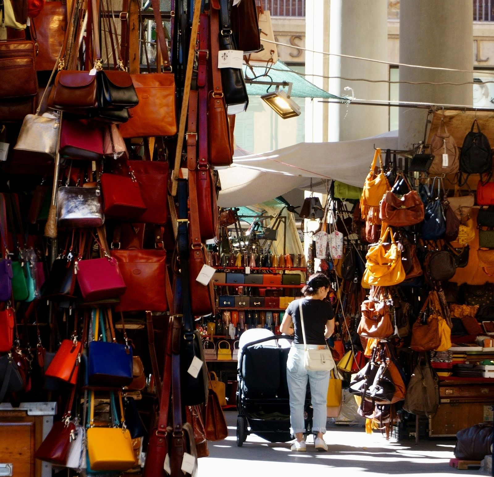 A woman shopping at a street store for bags with many shops having bags in view.