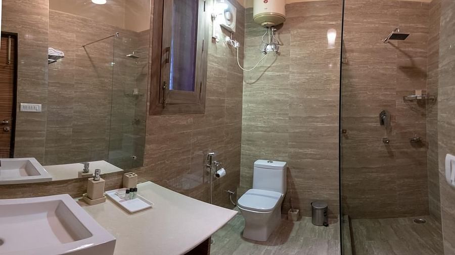 Bathroom with a large mirror, sink, toilet, and glass-enclosed shower, showing light-coloured tiled walls.