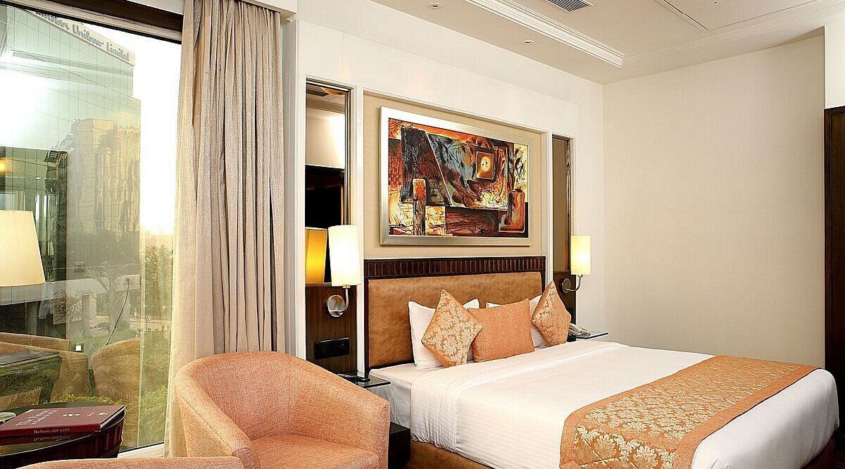 Executive Room with a double bed, bedside table with a lamp on top, cushioned seating with a table in front, and a window behind at Inde Signature Tower, Gurgaon