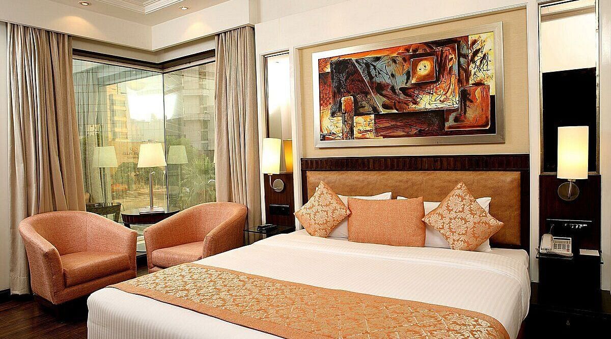 Executive Room with a double bed, bedside table with a lamp on top, cushioned seating with a table in front, and a window behind at Inde Signature Tower, Gurgaon