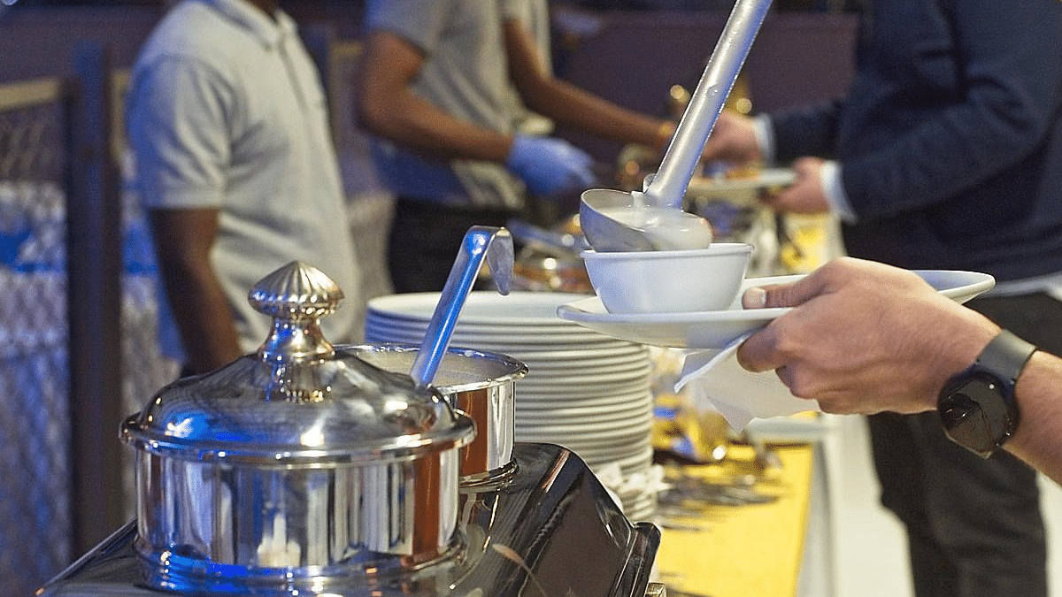 People serving food from chafing dishes at a buffet, hands and utensils visible.