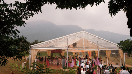 An outdoor event with guests gathered near a clear marquee tent, surrounded by nature and mountains in the background, creating a scenic and festive atmosphere at Black Thunder, Coimbatore