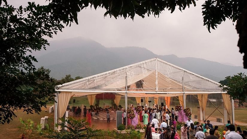An outdoor event with guests gathered near a clear marquee tent, surrounded by nature and mountains in the background, creating a scenic and festive atmosphere at Black Thunder, Coimbatore