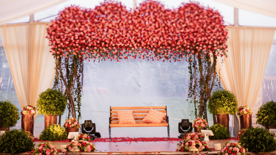 Beautifully decorated wedding stage with a floral arch in shades of pink and red, flanked by plants and flowers, set for a special ceremony at Black Thunder, Coimbatore