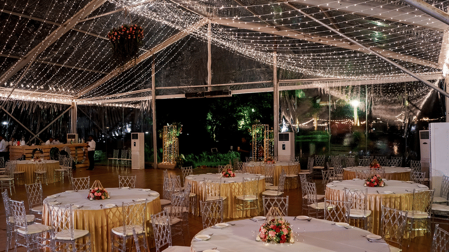 Indoor banquet setup under a beautifully draped ceiling with twinkling lights and round tables elegantly arranged with floral centrepieces at Black Thunder, Coimbatore