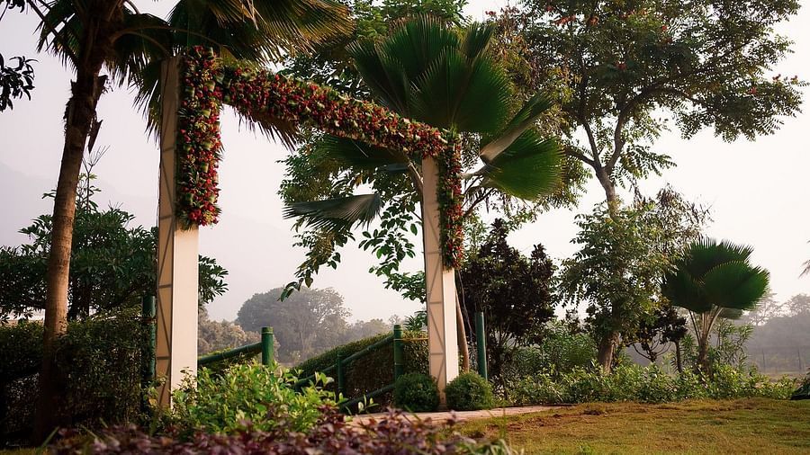 Outdoor event setup with lush greenery and palm trees, featuring floral-decorated columns and a walkway leading to the event area at Black Thunder, Coimbatore