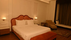 Suite at Mukundra Sarovar Premiere with a large bed, clean linens, a wooden headboard, an armchair, and a window bench with curtains.