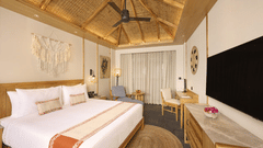 Room with double bed, fan, television, and bedside lamps in warm tones - Royal Tulip, Chitwan