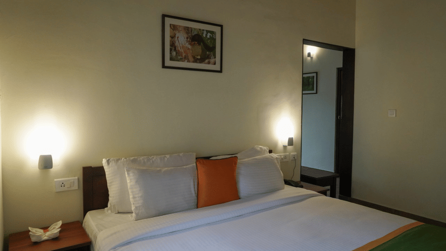 A bedroom features a neatly made-up bed and a lamp, offering a comfortable space.- Abad Brookside Lakkidi, Wayanad