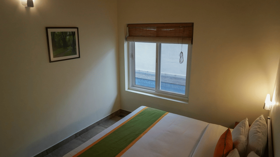 A bedroom features a made-up bed and a window, offering a comfortable space.- Abad Brookside Lakkidi, Wayanad