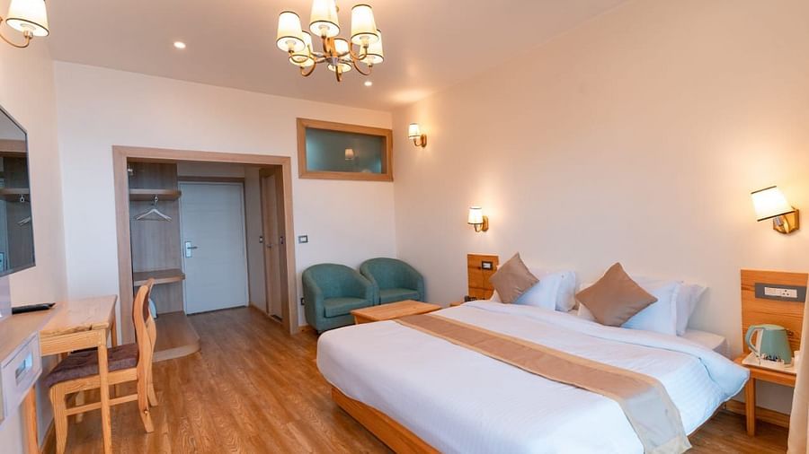 A bedroom with a bed, a chair, and a desk, warm lighting - Clarks Exotica Resort, Near Mukhteshwar.