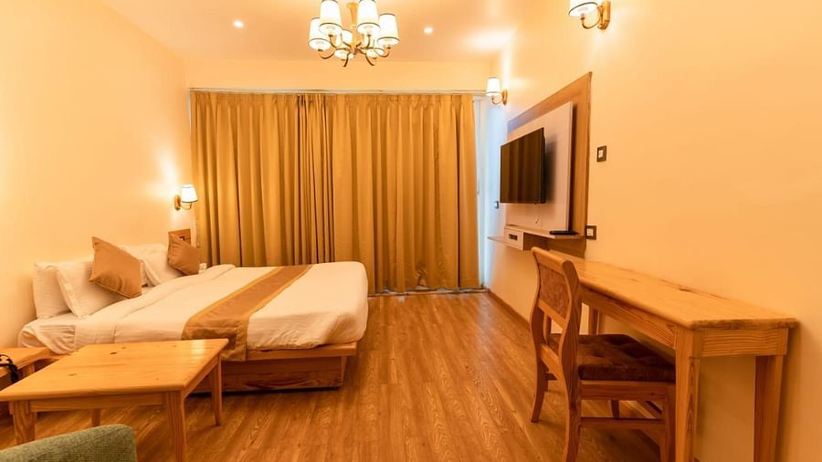 A bedroom with a bed, a couch, a desk, and a television, demonstrating a comfortable living space - Clarks Exotica Resort, Near Mukhteshwar.